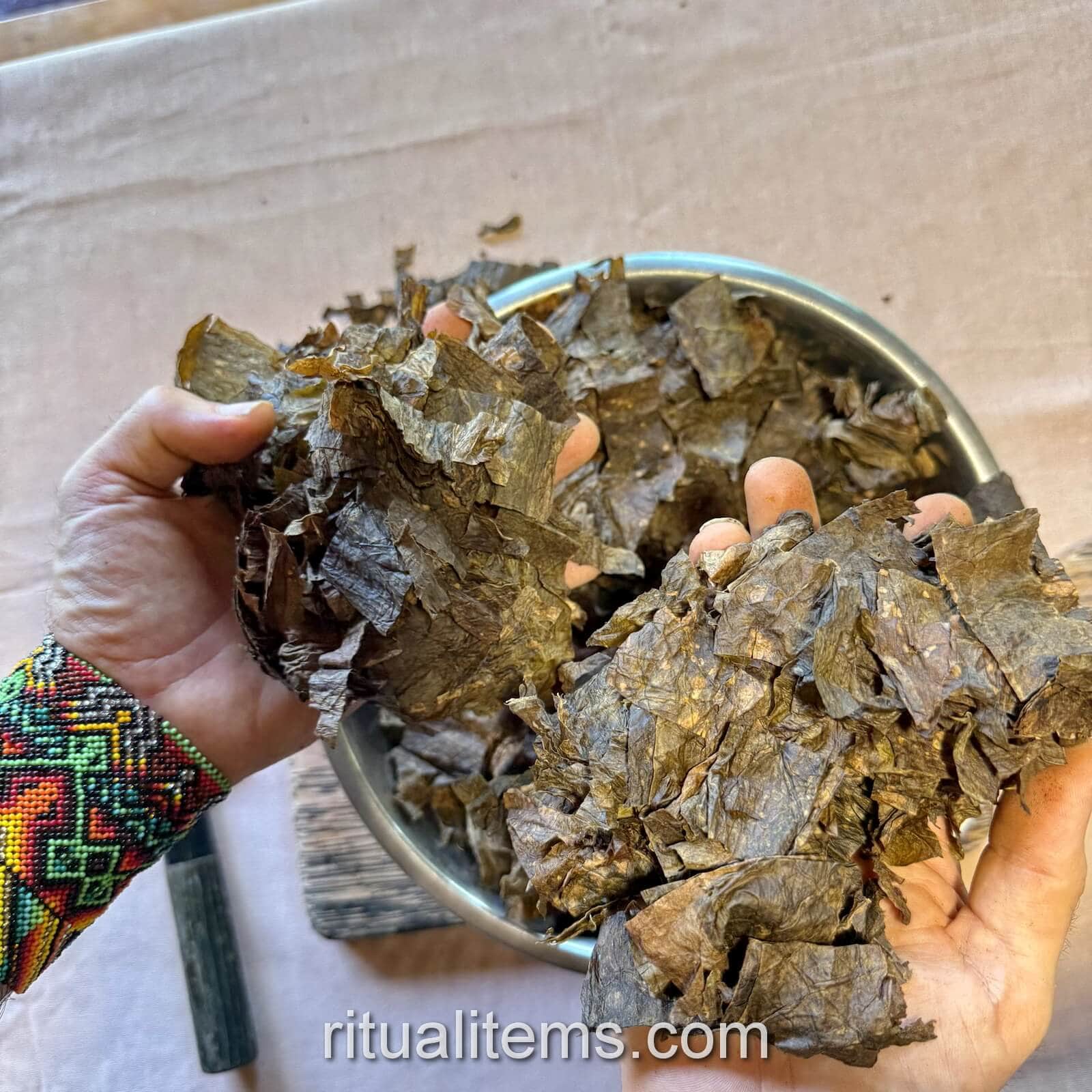 Two handfuls of broad Mapacho leaf pieces held above a metal bowl.