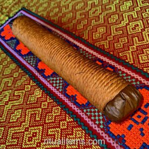 A brown wrapped Mapacho roll resting diagonally on a colorful woven textile.
