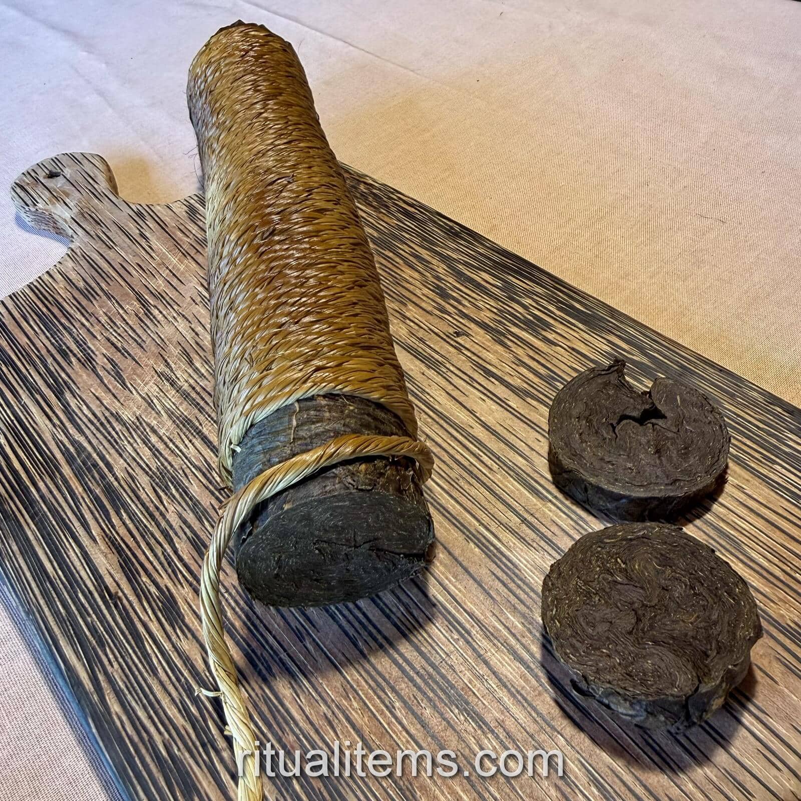 A wrapped Mapacho roll with two round slices on a wooden cutting board.